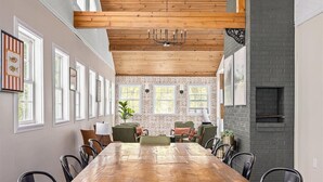 A long wooden dining table with chairs, a ceiling fan, and a brick wall with a fireplace. - 9BR Riverfront Estate | Pool, Theater, Game Room, on Shenandoah River (Shenandoah)