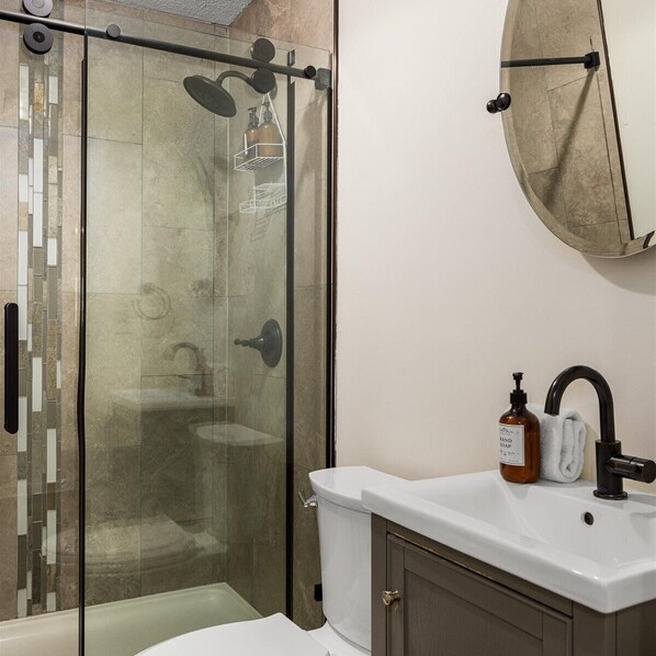 Un baño con cabina de ducha de vidrio, un lavabo blanco y un espejo sobre él.