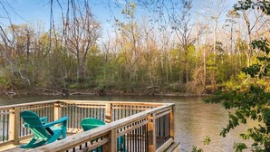 A wooden deck with chairs overlooking a calm body of water, surrounded by trees. - 9BR Riverfront Estate | Pool, Theater, Game Room, on Shenandoah River (Shenandoah)