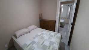 A bedroom with a bed, a wooden dresser, and a door leading to another room.