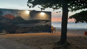 Ein Wandgemälde an einer Strandmauer zeigt einen Wal und Palmen, in der Nähe befinden sich ein Stuhl und ein Baum.