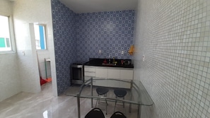 A compact kitchen with patterned blue and white tiles, a stainless steel oven, a sink, and a glass table with two stools.