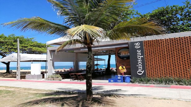 Ein Restaurant direkt am Strand mit Terrassenplätzen, einer Palme und Blick aufs Meer.