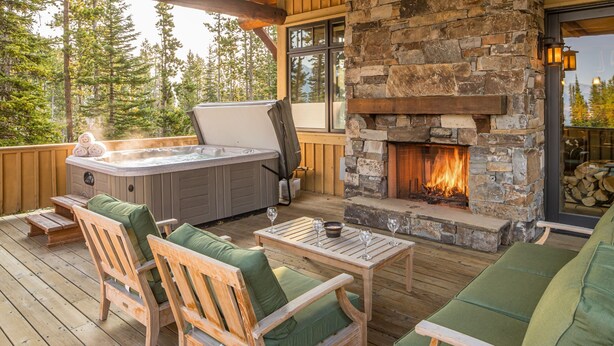 Una terraza de madera con mobiliario exterior, una chimenea de piedra y un jacuzzi.