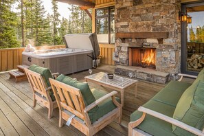 Une terrasse en bois avec des sièges d’extérieur, une cheminée en pierre et un jacuzzi.