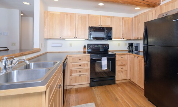 A modern kitchen with wooden cabinets, stainless steel appliances, and a black refrigerator.