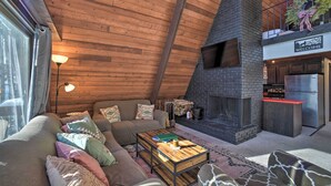 Un interior con techo de madera, chimenea, sofá, mesa de centro y zona de cocina.