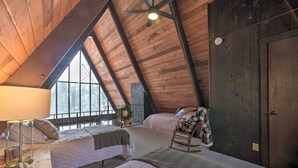 Un dormitorio acogedor en el ático, con dos camas, techo de madera y ventanas grandes.