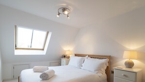 A neatly made bed with white linens and two rolled towels, a bedside lamp, and a nightstand with a lamp. - Adelaide Place (Canterbury)