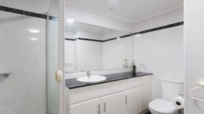 Et moderne badeværelse med en glasbrusekabine, en hvid vask med sort bordplade og et hvidt toilet.