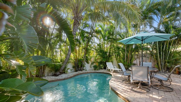 Ein Swimmingpool, umgeben von üppiger tropischer Vegetation, mit einer Terrasse, die mit Stühlen und einem Tisch ausgestattet ist.