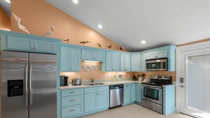 Uma cozinha moderna com armários verde-água, eletrodomésticos de aço inoxidável e arte decorativa na parede.