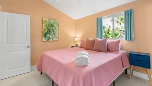 Quarto com cama, ventilador de teto, janela com cortinas, mesa de cabeceira e porta.