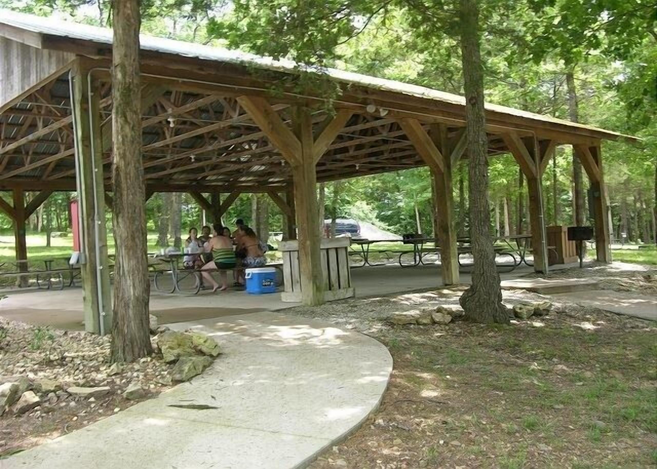 A covered picnic area with benches and picnic tables, surrounded by trees.