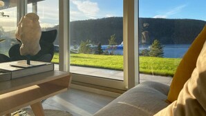 A modern living room with a large window offering a view of a lake and forest. - Cabin Oslofjord -sleeps14-seaview-familyfriendly (Frogn)