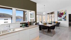A modern kitchen with large windows, a dining area with a table and chairs, and a view of the outdoors. - Cabin Oslofjord -sleeps14-seaview-familyfriendly (Frogn)