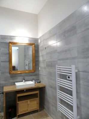 Une salle de bain avec un meuble-lavabo en bois, un lavabo blanc, un miroir à cadre doré et un porte-serviettes blanc.