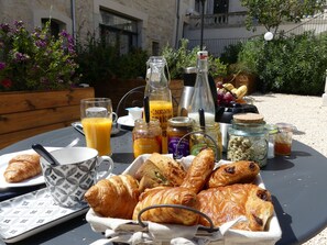 Un plateau de petit-déjeuner avec des croissants, du jus et divers accompagnements, disposé sur une table à l’extérieur.