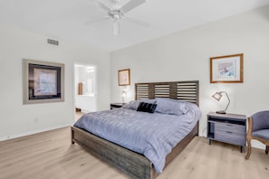 Une chambre à coucher avec un lit, une table de chevet, une chaise et un ventilateur de plafond.