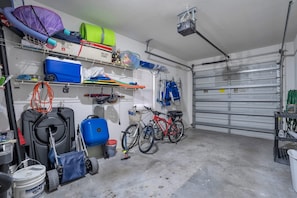 Eine Garage mit Fahrrädern, einem blauen Wagen und verschiedenen Werkzeugen auf Regalen.