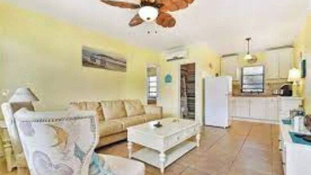 Ein Wohnzimmer mit Sofa, Couchtisch und Deckenventilator. Im Hintergrund ist eine Küchenzeile erkennbar.