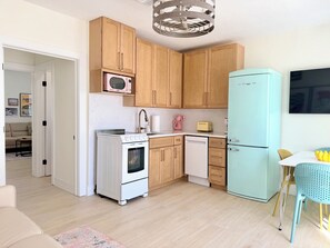 Une cuisine compacte avec des meubles en bois, un poêle blanc, un réfrigérateur bleu clair et un coin repas comprenant une table et des chaises.