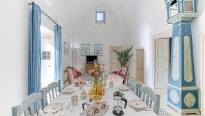 Une salle à manger avec une longue table dressée pour un repas, des chaises, un sol à motifs bleus et blancs et une haute colonne peinte en bleu et blanc.