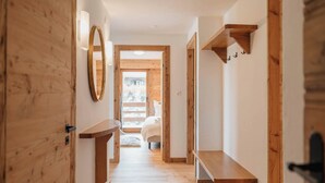 A wooden interior hallway with a bed visible through an open door at the end.