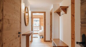 A wooden interior hallway with a bed visible through an open door at the end.