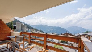 A balcony with a view of mountains, a wooden railing, and a table with chairs.