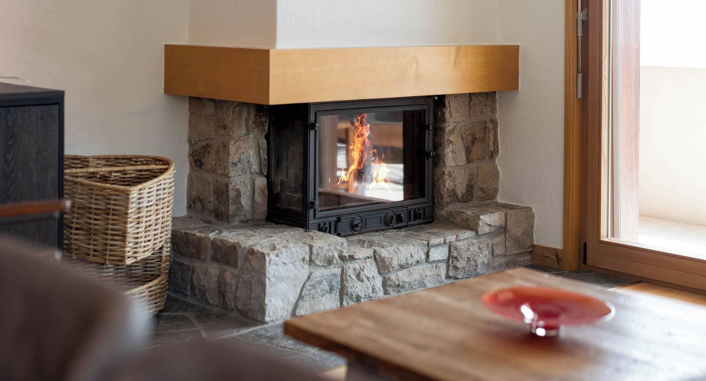 A stone fireplace with a modern design, a wicker basket, and a wooden table with a glass object on it.
