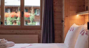 A hotel room with a bed, a window with curtains, and a view of a building with red flowers.