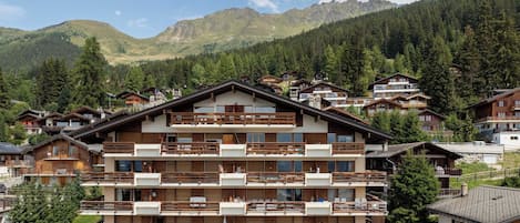 A multi-story hotel with balconies, set in a mountainous area with dense forest.
