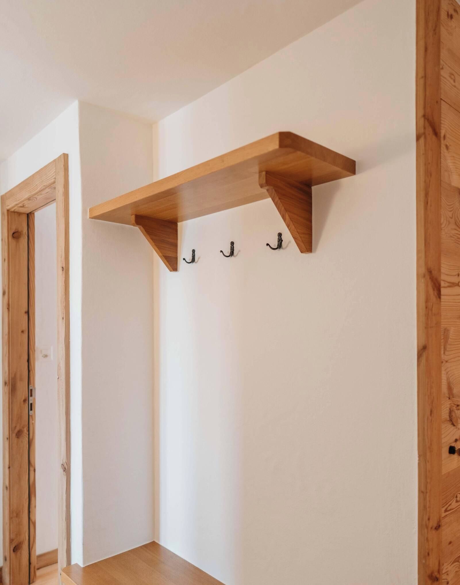 Une pièce d’angle avec une étagère en bois et trois crochets au mur.