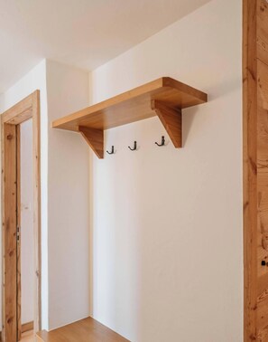A corner room with a wooden shelf and three hooks on the wall.