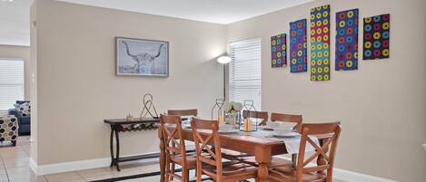 A dining area with a wooden table and chairs, a black and white rug, and a wall with colorful circular patterns.