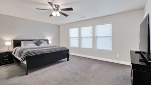 A bedroom with a bed, a nightstand, a ceiling fan, and a TV.