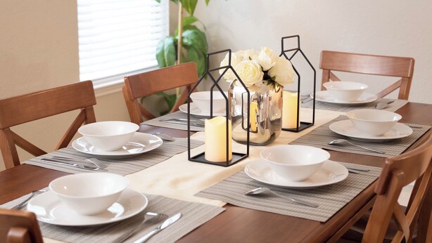 A dining table set with white bowls, plates, and cutlery, surrounded by wooden chairs.