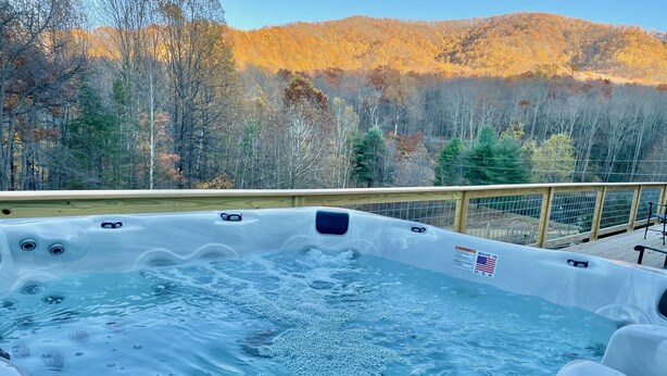Un bain à remous avec une terrasse en bois et une vue sur une montagne boisée.