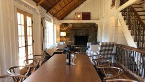 Une table à manger en bois avec des chaises, une cheminée en pierre et un escalier avec des rampes en bois.