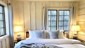 Une chambre avec un grand lit, deux lampes de chevet, une fenêtre donnant sur la forêt et des lambris en bois sur les murs.