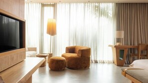 A modern hotel room with a flat-screen TV, a sofa, a chair, a desk, and a lamp. - 23 Hotel (Medellín)