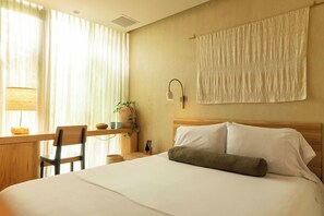 A hotel room with a bed, a desk, a chair, a lamp, a wall-mounted towel, and a plant. - 23 Hotel (Medellín)