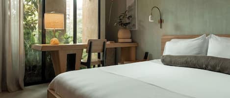Habitación de hotel con una cama grande, un escritorio con lámpara, una silla y vistas al exterior a zonas verdes.