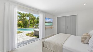 Un dormitorio con una cama grande, un televisor montado en la pared y una puerta corrediza que da a una zona de piscina.