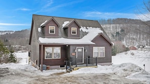 A two-story house with a dark brown exterior, a front porch with a railing, and a visible mailbox. - Northwood Chalet , exceptional view, 1mi to Village, Hot tub , A/C , fire pit (Ellicottville)
