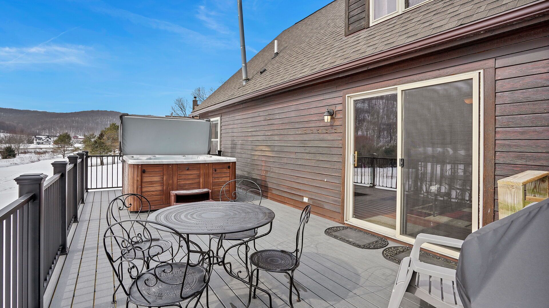 A wooden deck with a hot tub, a table, and chairs.