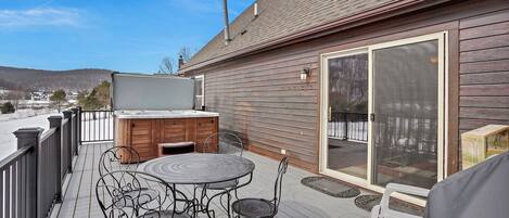 A wooden deck with a hot tub, a table, and chairs.
