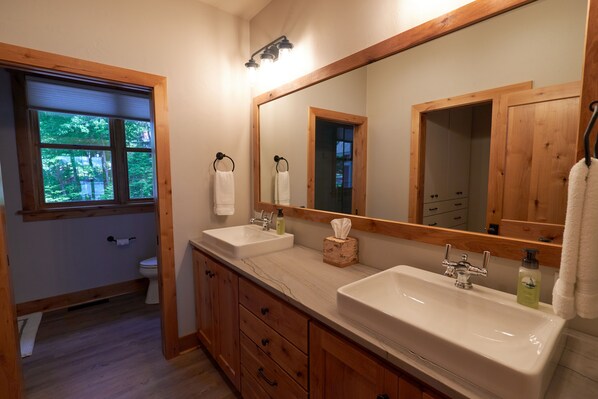 A bathroom with two sinks, a large mirror, and a window with a view of trees.