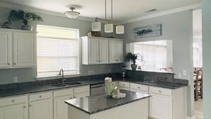 A kitchen with white cabinets, a granite countertop, a central island, and a trash bin. - Destined for Fun, House, Cabana, Pool + few steps to beach (Destin)